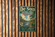 A vintage metal sign for De Soto National Forest in Mississippi, featuring a scenic landscape with a river, trees, and a waterfall.
