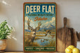 A vintage-style metal sign with a deer and ducks in a grassy field, mounted on a wall next to a wooden cutting board and a potted plant.