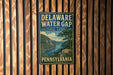 A vintage-style sign for the Delaware Water Gap in Pennsylvania, featuring a scenic landscape with a river and mountains.