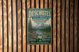 A vintage metal sign for the Deschutes National Forest in Oregon, featuring a scenic mountain landscape and the text "DESCHUTES NATIONAL FOREST OREGON EXPLORE DISCOVER Where Adventure Awaits".