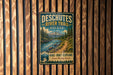 A vintage metal sign for the Deschutes River Trail in Oregon, featuring a scenic mountain landscape and a river.