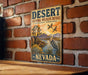 A vintage-style metal sign with a desert landscape and wildlife, mounted on a brick wall.