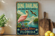 A vintage-style sign for the Sanibel Island Wildlife Refuge in Florida, featuring illustrations of a pink egret and a pelican.