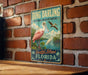 A vintage-style sign for the National Wildlife Refuge in Sanibel Island, Florida, featuring a pink flamingo and other birds in a tropical setting.