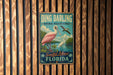 A vintage-style metal sign with a pink flamingo and text that reads "Ding Darling National Wildlife Refuge Sanibel Island Florida".