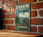 A vintage metal sign for the Dixon Memorial State Forest in Georgia, featuring a scenic illustration of a forest and a lake.