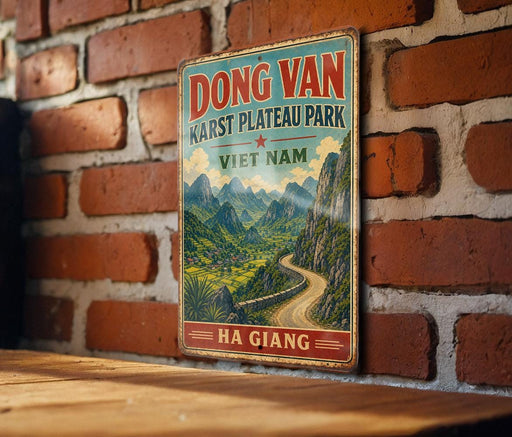 A vintage-style metal sign with a scenic mountain landscape and a winding road, mounted on a brick wall.