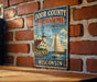 A vintage-style metal sign with a sailboat and lighthouse, mounted on a brick wall.