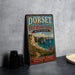 A vintage metal sign for the Dorset and East Devon Coast in the United Kingdom, featuring a scenic image of the Jurassic Coast and the surrounding landscape.