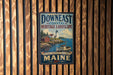 A vintage-style metal sign with the text "Down East Coastal Heritage Landscape" and "Wild Coast, Rich Heritage, Timeless Beauty, MAINE" is displayed on a wooden wall.