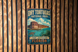 A vintage-style metal sign for Dry Tortugas National Park in Fort Jefferson, Florida, featuring an illustration of a building and a turtle in the water.