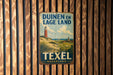 A vintage metal sign with the text "Duinen en Lage Land" and "Texel Nederland" hangs on a wooden wall.