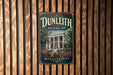 A vintage-style sign for Dunleith Historic Inn in Mississippi, featuring a large image of a historic building surrounded by trees and flowers.
