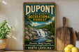 A vintage-style sign for DuPont State Recreational Forest in Brevard, North Carolina, featuring a waterfall and forest landscape.