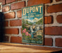 A vintage-style sign for DuPont State Recreational Forest, featuring a scenic illustration of a waterfall surrounded by lush greenery and pink flowers.