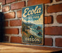 A vintage-style metal sign for Eola State Park in Oregon, featuring a scenic coastal landscape with mountains, water, and pine trees.