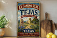 A vintage-style metal sign for the El Camino Real, a historic trail in Texas, featuring a scenic illustration of a historic building and a path leading through a garden.