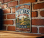 A vintage-style metal sign for the El Camino Real trail in Texas, featuring a scenic illustration of a historic landmark and the text "El Camino Real de los Tejas Heritage Trail" and "Texas A Historically Route, A Proud Heritage. Discover the Legacy".