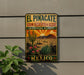 A vintage-style metal sign with a desert landscape and cacti, mounted on a wall next to a plant.