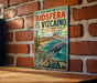 A vintage-style metal sign with a colorful illustration of a whale and desert landscape, mounted on a brick wall.