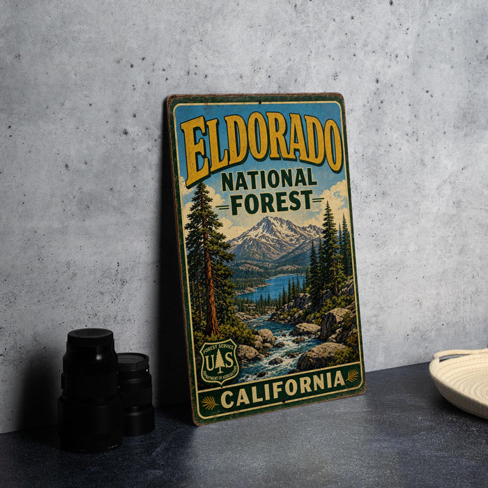 A vintage-style metal sign for the Eldorado National Forest in California, featuring a scenic landscape with mountains, pine trees, and a river.