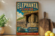 A vintage-style metal sign advertising the Elephant Caves in India, featuring a large image of a temple and a boat on the water.