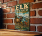 A vintage-style metal sign for the Elk State Forest in Pennsylvania, featuring an illustration of a large elk in a forest setting.