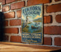 A vintage-style metal sign for the Elkhorn Slough National Estuarine Research Reserve in California, featuring an illustration of a heron and a beaver in a grassy area with a river and mountains in the background.