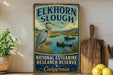 A vintage-style sign for the National Estuarine Research Reserve in California, featuring an illustration of a heron and a beaver in a river setting.