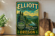 A vintage-style metal sign for Elliott State Forest in Oregon, featuring a scenic landscape with pine trees and a river.