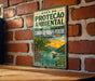 A vintage-style metal sign with text and an illustration of a tropical landscape, mounted on a brick wall.