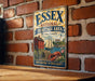 A vintage metal sign for the Essex National Heritage Area in Massachusetts, featuring an illustration of a red brick building, a lighthouse, and a lobster.