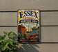A vintage metal sign for the Essex National Heritage Area in Massachusetts, featuring an illustration of a red brick house, a lighthouse, a sailboat, and other nautical elements.