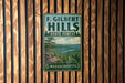 A vintage metal sign for F. Gilbert Hills State Forest in Massachusetts, featuring a scenic landscape with a river and mountains.