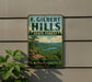 A vintage metal sign for F. Gilbert Hills State Forest in Massachusetts, featuring a scenic landscape with a mountain, lake, and pine trees.