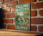 A vintage-style metal sign for Falling Waters State Park in Florida, featuring a waterfall and tropical foliage.
