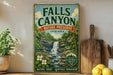 a vintage-style sign for Falls Canyon Nature Preserve, Indiana, with a waterfall and lush greenery. The sign is displayed on a shelf next to a wooden cutting board and a potted plant.