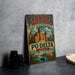 A vintage-style metal sign for the city of Ferrara, Italy, featuring a castle and a flamingo, is displayed on a gray countertop next to some black camera lenses.