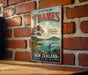 A vintage-style sign for the Firth of Thames, a famous tourist destination in Thames, England. The sign features a scenic image of the Thames River and the surrounding landscape, along with the text "Firth of Thames" and "Getting to the Coromandel Peninsula".