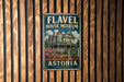 A vintage-style metal sign for the Fl aval House Museum in Astoria, Oregon, featuring an illustration of a Victorian-style house surrounded by flowers.
