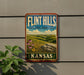 A vintage-style sign for "Flint Hills Cultural Landscape Kansas" is displayed on a wall, featuring a scenic landscape with grassy hills, flowers, and a blue sky with clouds.