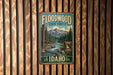 A vintage-style metal sign for the Floodwood State Forest in Idaho, featuring a scenic illustration of a forest and a river.