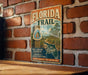 A vintage-style metal sign for the Florida Trail, featuring a scenic illustration of a trail surrounded by palm trees and a house, mounted on a brick wall.
