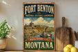 A vintage-style sign for Fort Benton National Historic Landmark in Montana, featuring a castle, river, and steamboat, with the text "Fort Benton Montana" and "Where history lives" below.