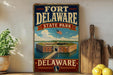 A vintage-style sign for Fort Delaware State Park, featuring an illustration of the fort and a flag, is displayed on a shelf next to a wooden cutting board and some lemons.