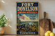 A vintage-style sign for Fort Donelson National Battlefield in Tennessee, featuring an American flag and a cannon, is displayed on a shelf next to a wooden cutting board and some lemons.
