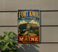 A vintage-style metal sign for Fort Knox, Maine, featuring a cannon and a building, is displayed on a gray wall.