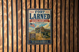 a vintage-style metal sign for the Fort Larned National Historic Site in Kansas, with an American flag and a cannon in the background.