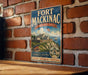 A vintage-style metal sign for Fort Mackinac, Michigan, featuring an illustration of the fort and surrounding landscape, mounted on a brick wall.