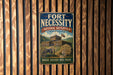 a vintage metal sign with the text "FORT NECESSITY" and "NATIONAL BATTLEFIELD - PENNSYLVANIA" displayed prominently. The sign also includes the phrase "WHERE HISTORY WAS MADE" and features an illustration of a cannon and a wooden fort.